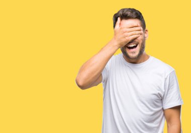 Yakışıklı genç gülümseyen ve gözler için sürpriz kapsayan yüz el ile gülüyor izole arka plan üzerinde. Kör kavramı.