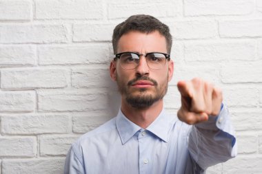 Kamera ve size, el işareti, pozitif ve kendinden emin bir jest ön parmak ile işaret beyaz tuğla duvarın üzerinden duran genç yetişkin iş adamı