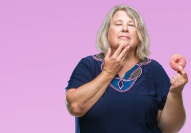 Kıdemli artı boyutu arka plan ciddi bir yüz hakkında soru, çok karışık bir fikir düşünce kafkas kadın üzerinde şeker donut yemek izole