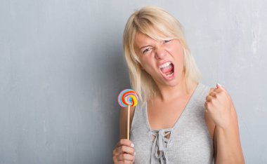 Candy lolipop yemek gri grunge duvarın üzerinden Kafkas yetişkin kadın rahatsız ve boşa çıkarmak ile öfke, çılgın da yükseltilmiş el ile bağırmaya kavramı öfke
