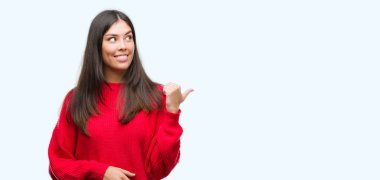 Kırmızı kazaklı seyir ve başparmak yanında yukarıyı mutlu yüz ile gülümseyen giyen genç güzel İspanyol.