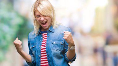 Üzerinde kot ceket giyen genç güzel sarışın kadın gülümseyerek ve başarı için çığlık arka plan çok mutlu ve heyecanlı kaldırdı, silah ile kazanan jest yapıyor izole. Kutlama kavramı.