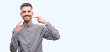 Kendinden emin gösterilen ve işaret parmakları diş ve ağız ile gülümseyen genç hipster adam. Sağlık kavramı.