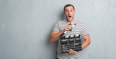 Beyaz delikanlı film fıçı tahtası korkmuş şok bir sürpriz yüz, korkuyor ve heyecanlı korku ifadesi ile tutarak gri grunge duvarın üzerinden