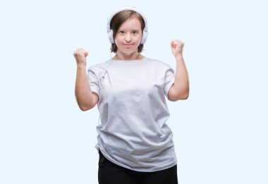 Down sendromlu üzerinde kulaklık giyen genç yetişkin kadın gülümseyerek ve başarı için çığlık arka plan çok mutlu ve heyecanlı kaldırdı, silah ile kazanan jest yapıyor izole. Kutlama kavramı.