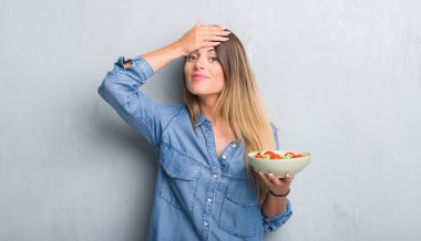 Baş, el ile vurguladı sağlıklı domates salatası yemek gri grunge duvarın üzerinden Genç Yetişkin kadın şok utanç ve sürpriz suratla, öfkeli ve sinirli. Korku ve hata için üzgün.