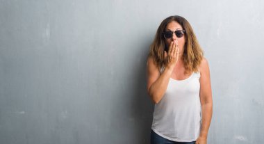 Orta yaş İspanyol kadın güneş gözlüğü takıyor gri duvarın üzerinden el ile ağız kapsayan yorgun esneme sıkılmış. Restless ve uyku hali.