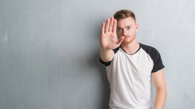 Elin avuç durağı şarkı yapıyor gri grunge duvarın üzerinden genç Kızıl saçlı adam. Negatif ve ciddi bir jest yüz ifadesiyle uyarı.