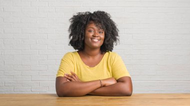 Ev mutlu yüz çapraz silah kameraya bakarak ile gülümseyen masada oturan genç Afro-Amerikan kadın. Olumlu bir kişi.