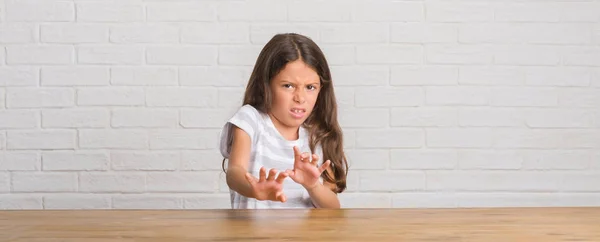 年轻的西班牙裔孩子坐在家里的桌子上厌恶表情 不高兴和害怕做厌恶的脸 因为厌恶反应 恼人的概念 — 图库照片