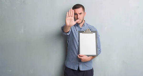 Joven Hombre Caucásico Sobre Pared Grunge Gris Sujetando Portapapeles Con —  Fotos de Stock