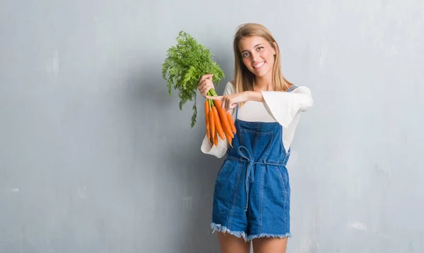 Vacker Ung Kvinna Över Grunge Grå Väggen Håller Färska Morötter — Stockfoto