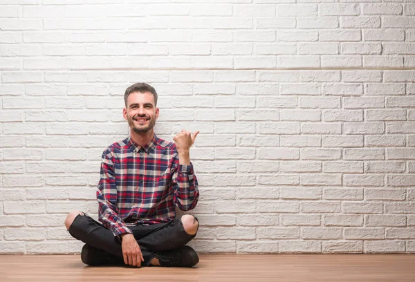 Homem Adulto Jovem Sentado Sobre Parede Tijolo Branco Apontando Mostrando — Fotografia de Stock