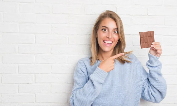 Mulher Bonita Sobre Parede Tijolo Branco Comer Barra Chocolate Muito — Fotografia de Stock