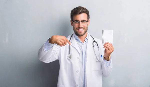 Handsome Young Doctor Man Grey Grunge Wall Holding Blank Notebook — Stock Photo, Image