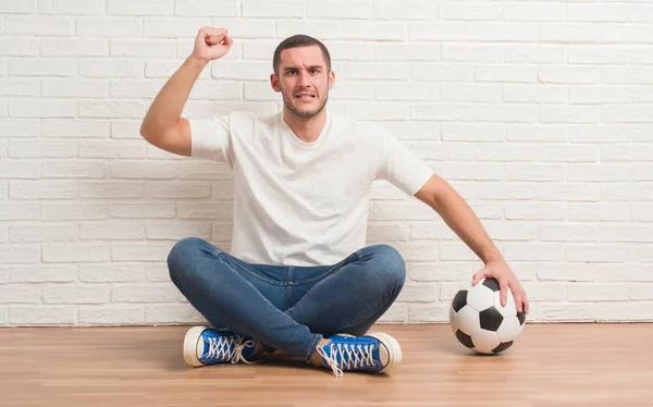 Καυκάσιος Νεαρός Κάθεται Πάνω Από Λευκό Τοίχο Κρατώντας Ποδόσφαιρο Ποδόσφαιρο — Φωτογραφία Αρχείου