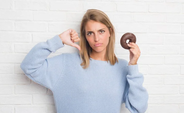 Красивая Молодая Женщина Стеной Белого Кирпича Ест Шоколадный Пончик Сердитым — стоковое фото