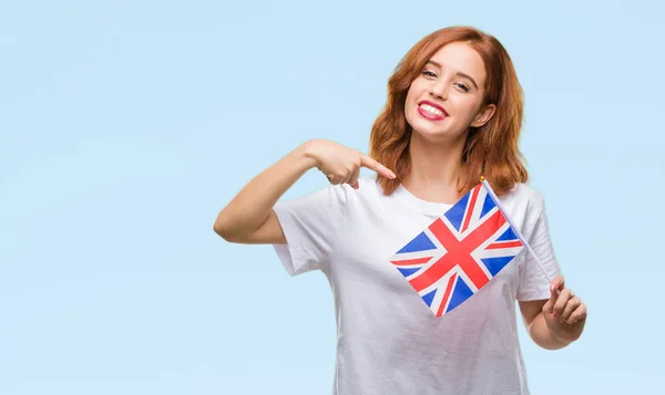 年轻美丽的妇女持有英国国旗在孤立的背景很高兴指着手和手指 — 图库照片