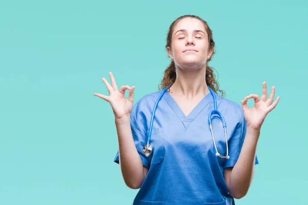 Young brunette doctor girl wearing nurse or surgeon uniform over isolated background relax and smiling with eyes closed doing meditation gesture with fingers. Yoga concept.