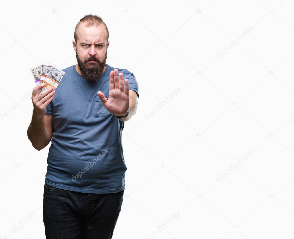 Young hipster man holding bunch of money over isolated background with open hand doing stop sign with serious and confident expression, defense gesture
