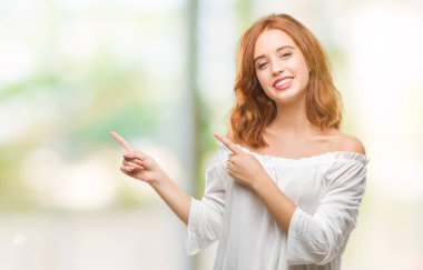 Gülümseyen ve iki elleri ve parmakları ile tarafına işaret kamera bakarak izole arka plan üzerinde genç güzel kadın.