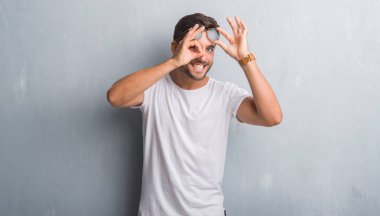 Yakışıklı genç gülümseyen, parmakları ile mutlu yüz üzerinden seyir göz el ile ok jest yapıyor güneş gözlüğü takıyor gri grunge duvarın üzerinden.