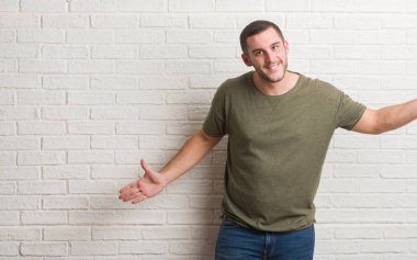 Sarılmak için kollarını açarak gülümseyerek kameraya bakarak beyaz tuğla duvarın üzerinden ayakta beyaz delikanlı. Neşeli ifade kucaklayan mutluluk.