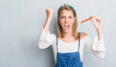 Güzel ve genç birbayan biberli pizza yeme grunge gri duvarın üzerinden dilim rahatsız ve hayal kırıklığı ile öfke, çılgın ve yükseltilmiş eliyle diye bağıran öfke kavramı bağırarak