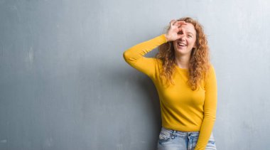 Genç Kızıl saçlı kadın gülümsüyor, parmakları ile mutlu yüz üzerinden seyir göz el ile ok jest yapıyor gri grunge duvarın üzerinden.