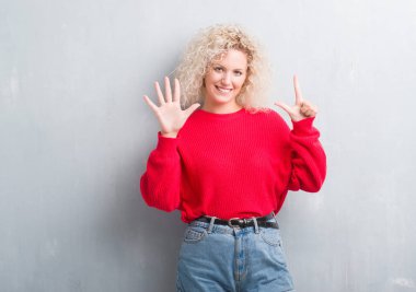 Gösterilen ve parmakları ile işaret grunge gri arka plan üzerinde Kıvırcık saçlı sarışın genç kadın kendinden emin ve mutlu gülümseyerek süre yedi numara.
