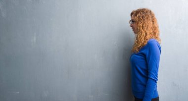 Genç Kızıl saçlı kadın tarafına, seyir gri grunge duvarın üzerinden dinlenmek doğal yüz emin gülümseme ile pozuyla profili.