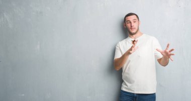 Şokta bağırarak Genç beyaz adam gri grunge duvar korkuyor ve dehşet korku ifade dur hareketi el ile ile güneş gözlüğü takıyor. Panik kavramı.