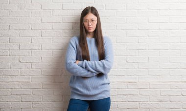 Beyaz tuğla duvar şüpheci ve sinir, onaylamayan ifade yüz çapraz kolları olan genç Çinli kadın. Negatif kişi.