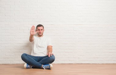 Beyaz delikanlı dur yapıyor beyaz tuğla duvardan katta oturan elin avuç ile şarkı. Negatif ve ciddi bir jest yüz ifadesiyle uyarı.