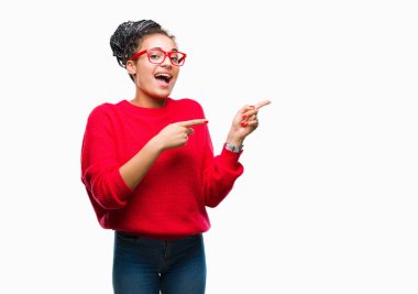 Genç gülümseyen ve iki elleri ve parmakları ile tarafına işaret kamera bakarak izole arka plan üzerinde saç Afro-Amerikan Kız giyiyor kazak ve gözlük örgülü.