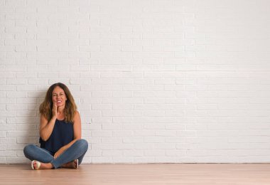 Orta yaş İspanyol kadın diş ağrısı veya dişlerde dişlerle ilgili hastalık nedeniyle ağız acı ifadesi ile el ile dokunmak beyaz tuğla duvarın üzerinden yere oturma. Diş hekimi kavramı.