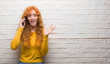 Tuğla üzerinde duran genç Kızıl saçlı kadın büyük gülümseme ile çığlık zaferini kutluyor telefon çok mutlu ve heyecanlı, kazanan ifade konuşurken duvar ve ellerini kaldırdı