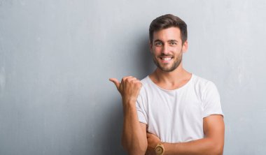 Yakışıklı delikanlı arıyor ve başparmak yanında yukarıyı mutlu yüz ile gülümseyen gri grunge duvarın üzerinden.