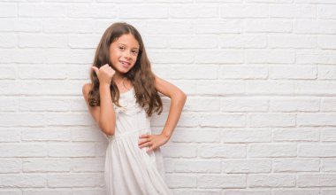 Beyaz duvara bakarak ve başparmak yanında yukarıyı mutlu yüz ile gülümseyen genç İspanyol çocuk.