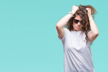 Güzel esmer kıvırcık saçlı Genç kız çünkü umutsuz ve stresli baş ağrısı acı izole arka plan üzerinde güneş gözlüğü takıyor ağrı ve migren. Ellerini kafasına.