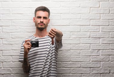 Vintage kamerayı kızgın yüzü, eksi işareti aşağı antipati başparmak ile gösterilen, ret kavramı ile beyaz tuğla duvar üzerinde duran genç adam