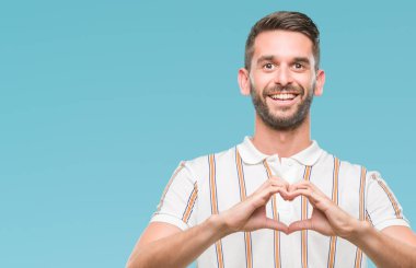 Yakışıklı delikanlı aşık kalp simgesi ve elleriyle şekil gösteren gülümseyen izole arka plan üzerinde. Romantik kavramı.