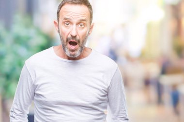 Orta yaş ağarmış komuta sizde korkmuş ve şok sürpriz ifade, korku ve heyecan yüz ile izole arka plan üzerinde beyaz t-shirt giyen.