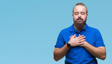 Genç beyaz hipster adam kapalı gözler ile göğüs ellerinde ve yüzünde minnettar jest ile gülümseyen izole arka plan üzerinde mavi tişört giyiyor. Sağlık kavramı.