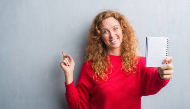 Gri grunge duvar gösteren boş dizüstü el ve parmak ile tarafına işaret çok mutlu genç Kızıl saçlı kadın