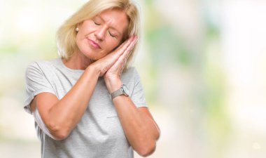 Orta yaş uyku yorgun hayal ve ellerle birlikte poz ile kapalı gözler gülümseyen izole arka plan sarışın kadın.