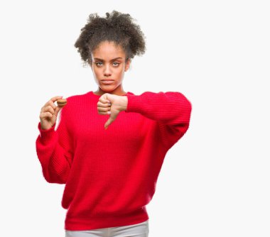 Kızgın yüz, eksi işareti aşağı antipati başparmak ile gösterilen, ret kavramı ile izole arka plan üzerinde çikolata macaron yeme genç afro Amerikalı kadın