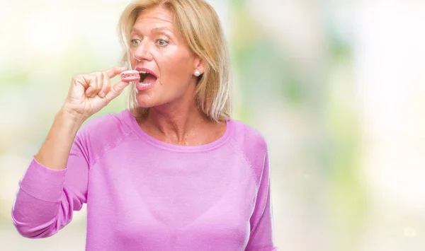 Mulher Loira Meia Idade Comer Biscoito Macaron Rosa Sobre Fundo — Fotografia de Stock
