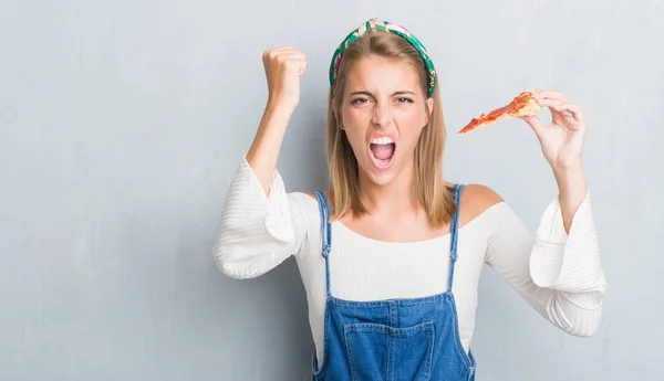 ペパロニのピザを食べるグランジ灰色の壁に美しい若い女性スライス イライラと不満の叫び狂気と上げられた手で 叫んで 怒りと怒りのコンセプト — ストック写真
