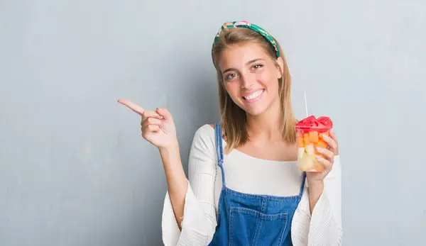 グランジ灰色壁側の手と指で指す非常に幸せな果物を食べる以上の美しい若い女性 — ストック写真
